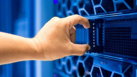 File image: Hand reaching toward server networking equipment in blue-lit data centre facility