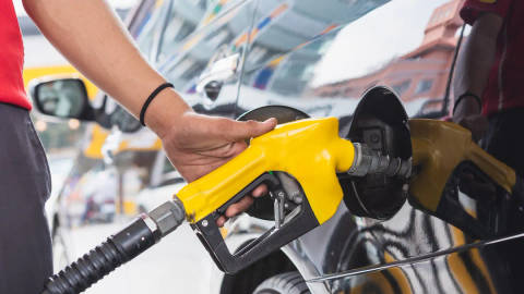 Person refueling vehicle with yellow nozzle at service station