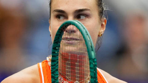 Tennis player holding green racket near face, wearing orange sports attire