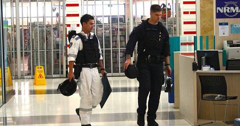Two uniformed personnel walking through indoor facility with glass doors and yellow wet-floor sign visible.