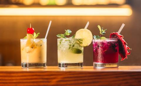 File image: Three professionally crafted cocktails displayed on a bar counter with warm lighting