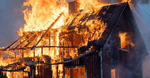 House fully engulfed in flames with fire consuming roof and windows