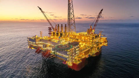 Illuminated offshore oil and gas production platform at sunset, surrounded by ocean.