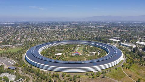 Aerial view of Apple Park, Apple's distinctive circular headquarters building in Cupertino, California, surrounded by green landscaping and trees.