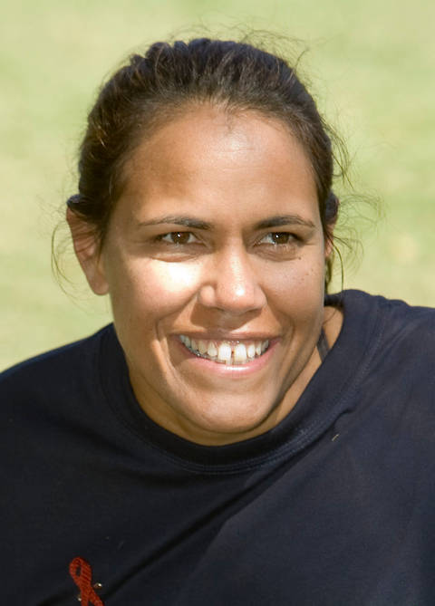 Cathy Freeman. A close-up photograph of a woman with dark hair pulled back, smiling broadly at the camera, wearing a dark top against a blurred green background.
