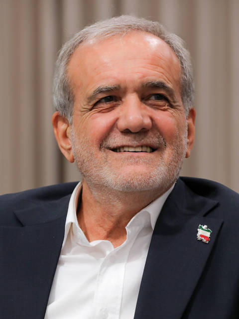 Masoud Pezeshkian. A grey-haired man with a short grey beard wearing a dark blazer over an open-collar white shirt and a small Iranian flag lapel pin, smiling broadly and looking slightly upward agai