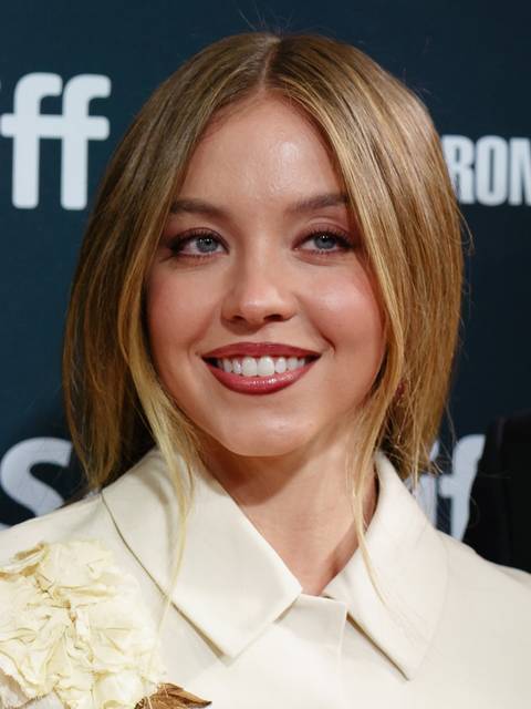 Sydney Sweeney. A young woman with shoulder-length blonde hair smiles at the camera wearing a cream blazer with floral detail at a TIFF event.