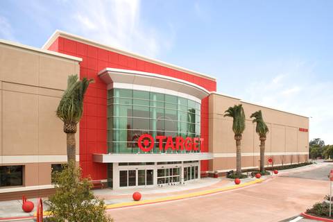 The exterior of a Target retail store with its red and tan facade, large glass entrance, prominent red Target logo and signage, palm trees, and an empty parking area in front.