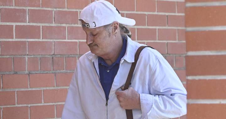 Rodney Joseph Minogue. Man in white cap and light jacket standing against red brick wall