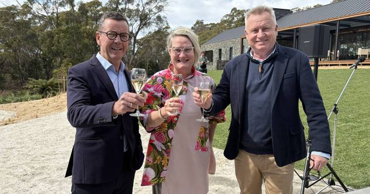 Three people in business casual attire toasting with champagne outside modern winery building with gum trees