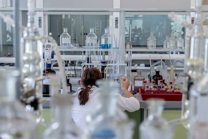 Researcher in white coat working with laboratory glassware and equipment at laboratory bench.