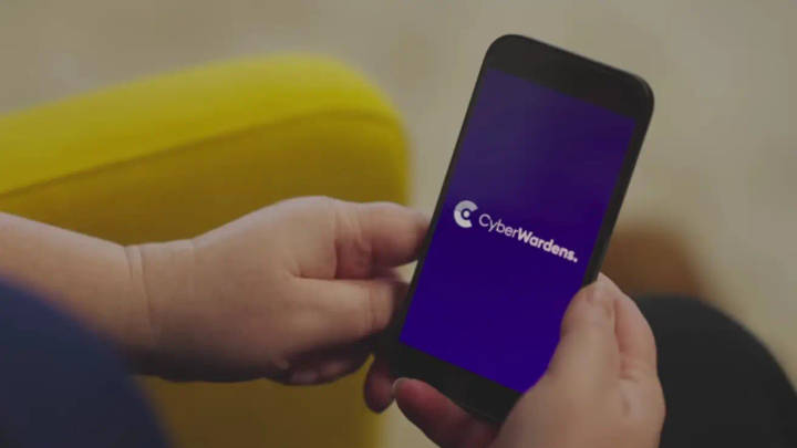 Person holding smartphone displaying CyberWardens logo on purple screen