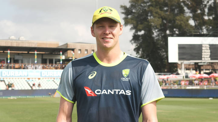 Australian cricketer in Qantas team uniform on cricket ground, smiling at camera