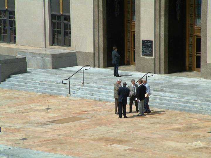 File image: Modern institutional building courtyard with steps and figures in business attire, formal legal setting.
