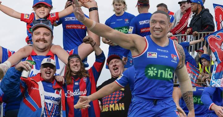 Newcastle Knights fans and players celebrating outdoors, group includes child on adult's shoulders, all wearing team jerseys