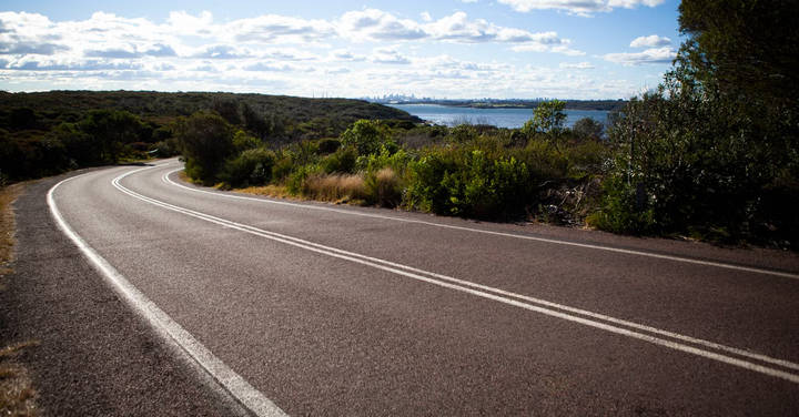 File image: Winding two-lane road through bushland beside a calm waterway