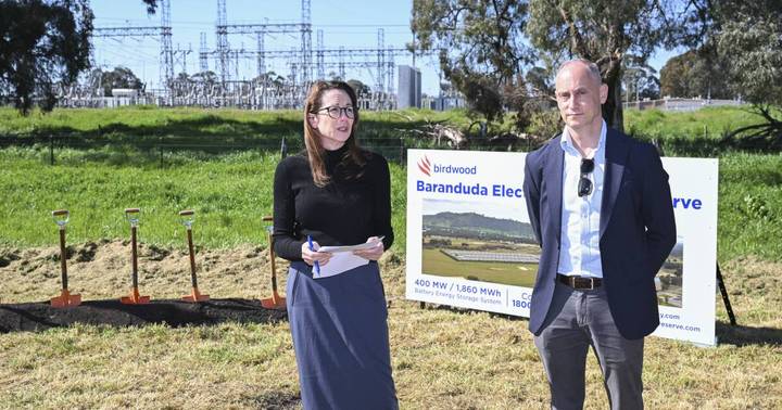 Two people presenting at renewable energy project event with power towers and promotional banner in regional Australian setting