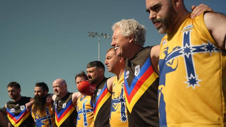 Group of adult men in yellow and blue AFL uniforms standing together outdoors