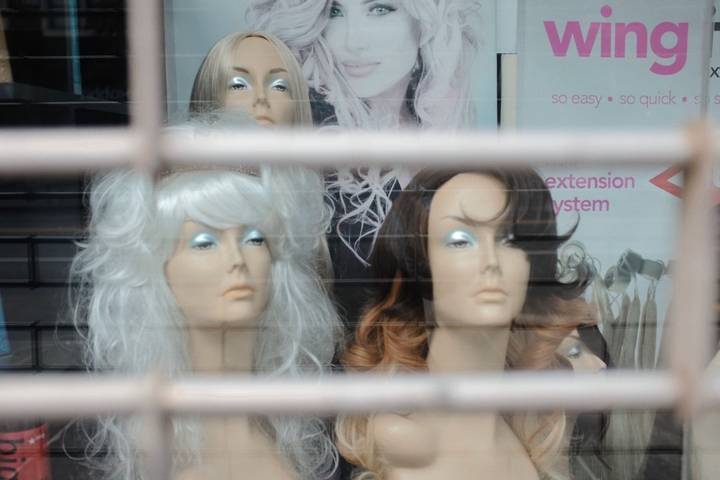 File image: Storefront window displaying mannequin heads wearing wigs with 'wing extension system' signage visible.