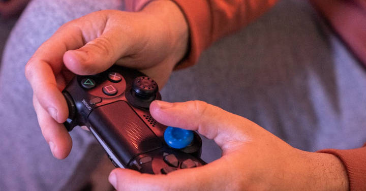 File image: Hands holding PlayStation controller in overhead lighting against dark background