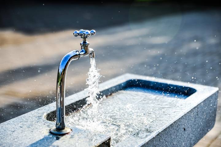 Water stream flowing from metal tap into basin outdoors