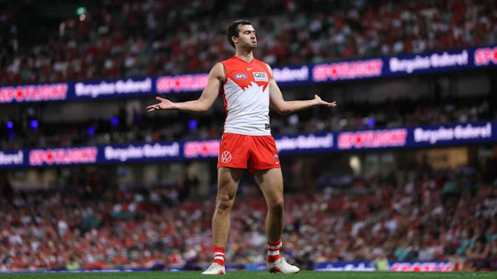 AFL player in red-and-white Swans uniform gestures during match at full stadium