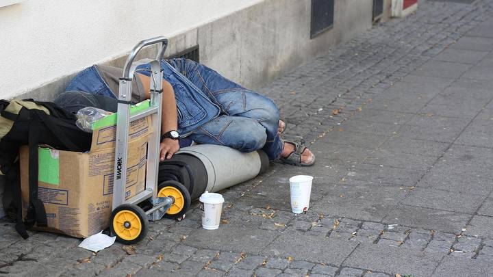Person on street with cardboard box and belongings illustrating homelessness context