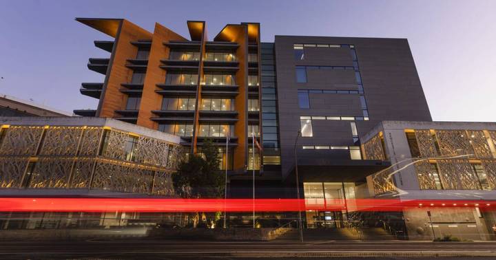 Modern multi-story building at dusk, orange and gray facades, decorative ground-level screens, red neon accent