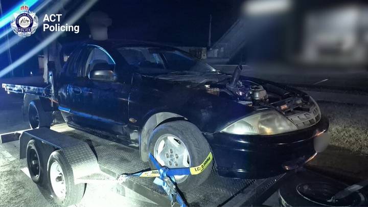 Towed dark vehicle with open door on flatbed at night, second vehicle visible, ACT Police branding