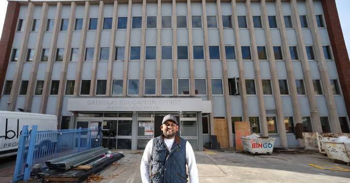 Blaq Projects. Man in cap and vest before Wollongong Catholic Education Office building under renovation with construction fencing