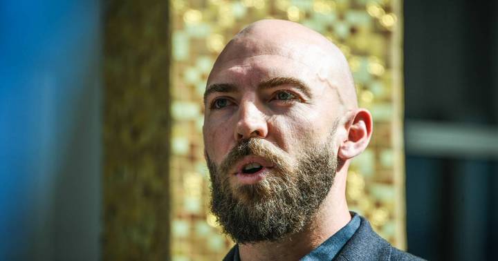 Thomas Emerson. Bald bearded man in dark shirt photographed outdoors against blurred foliage
