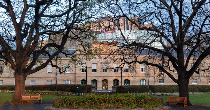 File image: Stone government building with large windows, bare trees, benches, manicured lawn