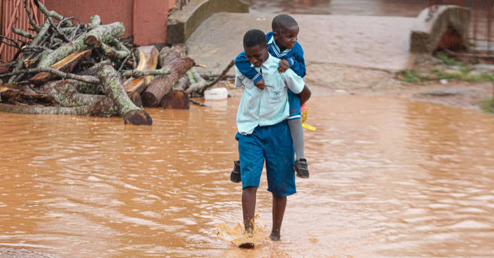 File image: Two children wading through brown flood water near buildings in tropical setting