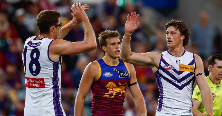 Brisbane Lions player in blue-maroon jersey surrounded by two Fremantle Dockers players in white-purple during AFL match