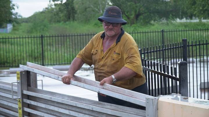 Man in work shirt at residential fencing with water and trees behind
