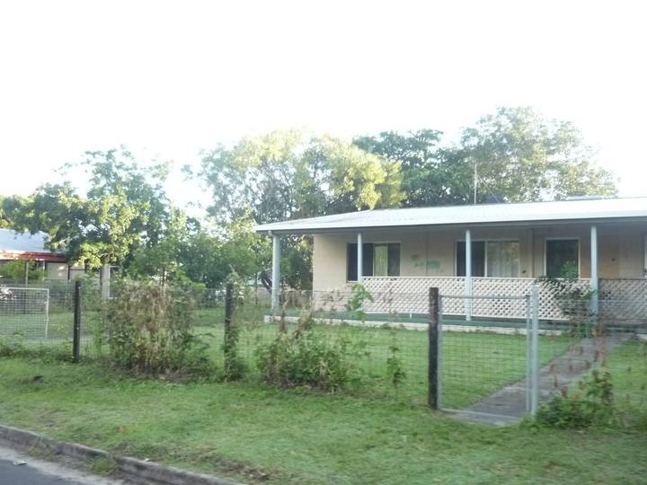 Single-story weathered Australian house with verandah, fenced yard and overgrown grass.