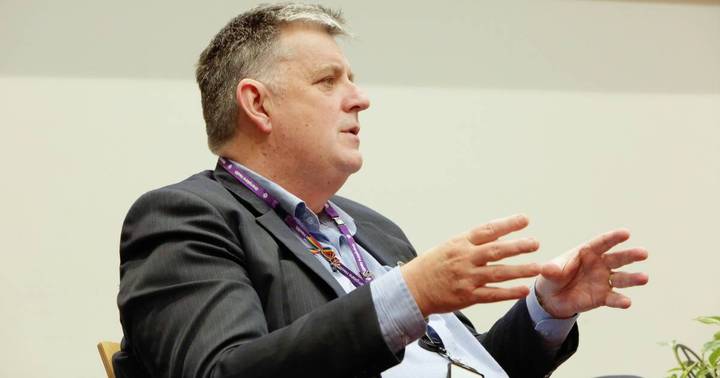 Dale Fraser. Professional speaker in dark suit gestures while addressing audience at event