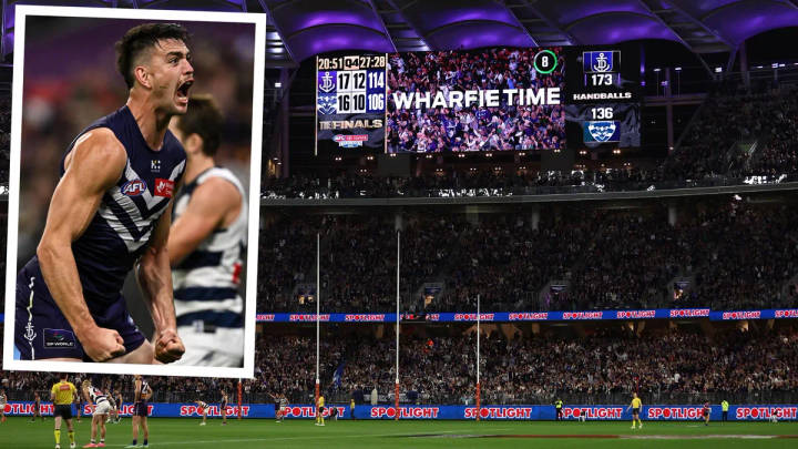AFL player celebrating in navy uniform; stadium scoreboard and crowd behind