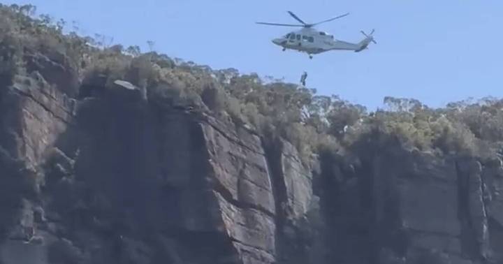 Helicopter hovering above rocky cliff as rescue operation takes place at Illawarra Escarpment