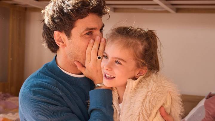 Man whispering to smiling young girl in home interior. Affectionate family moment between adult and child.