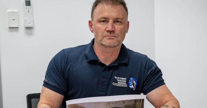 Mark Harriss. Man in dark blue organizational polo shirt seated indoors against white wall