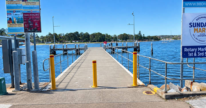 Concrete pier extending into blue water with yellow bollards and metal railings