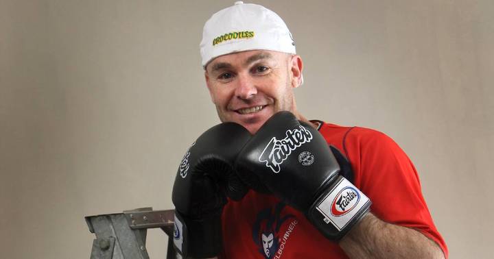 Rodney Ryan. Man in white cap and red shirt wearing black boxing gloves, smiling against neutral background