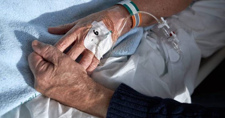 Elderly patient's hand wearing medical electrode patch in hospital bed