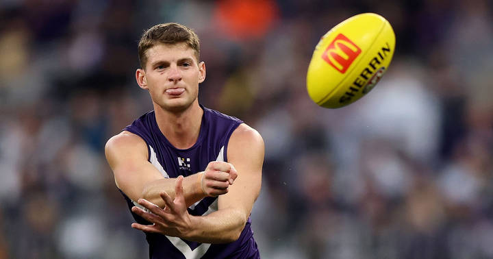Judd McVee. AFL player in purple Fremantle jumper reaching for ball during match