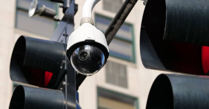 Dome surveillance camera mounted on pole above urban street with building background