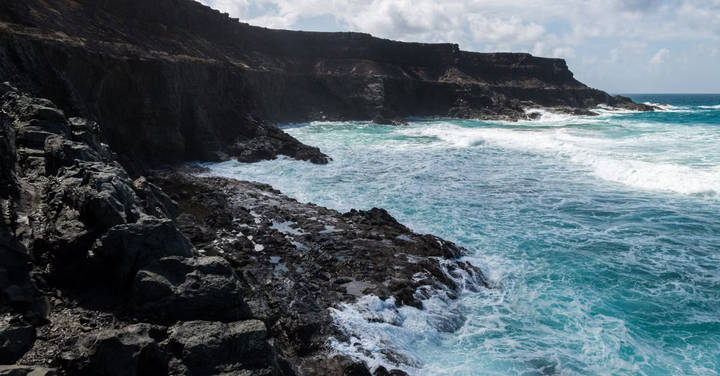 File image: Dark volcanic rocky coastline with turquoise waves and cliffs