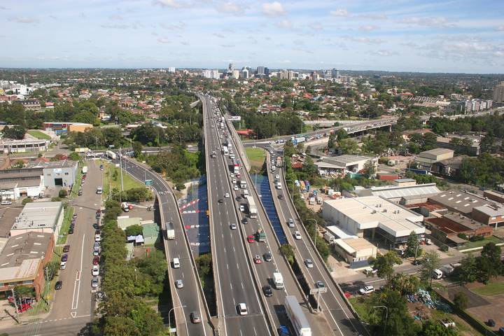 File image: Aerial view of multi-lane motorway with traffic through suburban landscape with city skyline.