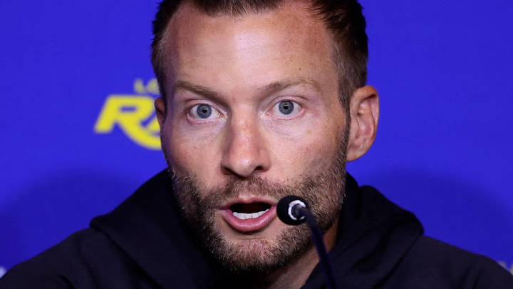 Bearded man speaking at microphone against blue background