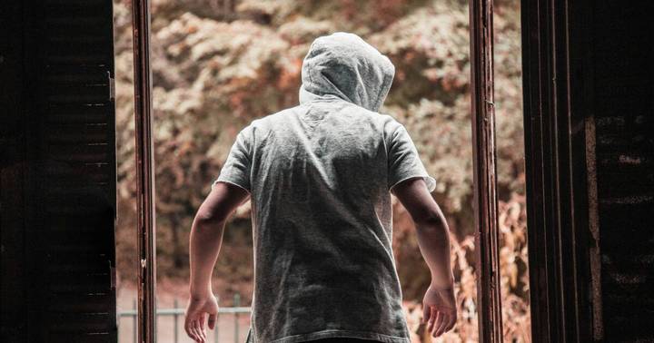 Person from behind in gray t-shirt and hood near brick building and metal railing